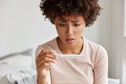 Confused woman looking at faint line on first response pregnancy test results