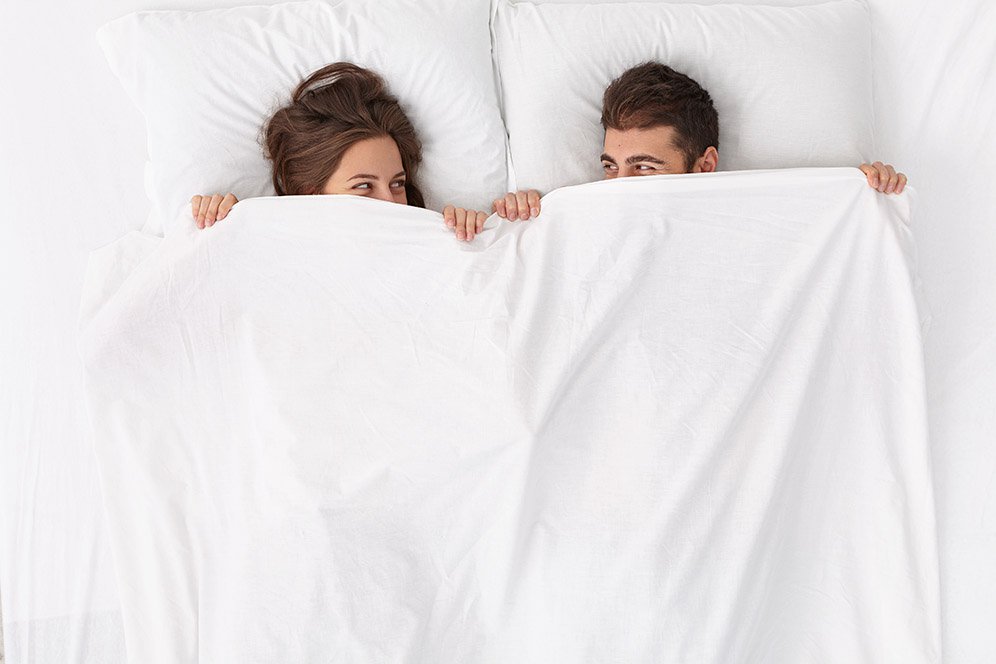 Loving couple sharing a playful moment in bed, wrapped in a blanket.