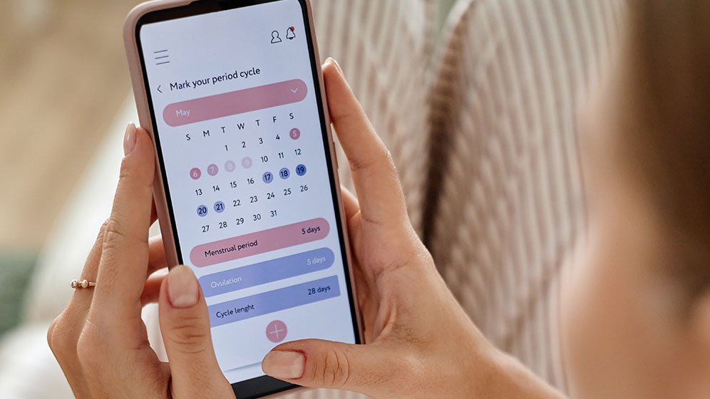 Adult woman holding smartphone, checking menstrual cycle tracking app while sitting.